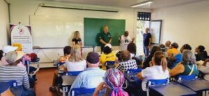 Sala de aula cheia de mulheres com um homem em pé e duas mulheres ao seu lado
