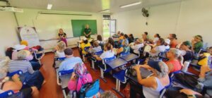 Sala de aula cheia de mulheres com um homem em pé e duas mulheres ao seu lado