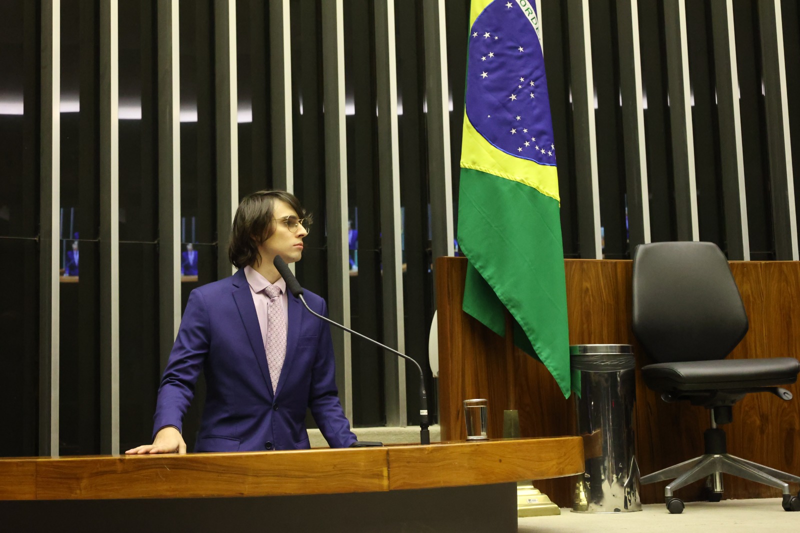 Deputado Amom na câmara em pé olhando para a bandeira do brasil às sua esquerda