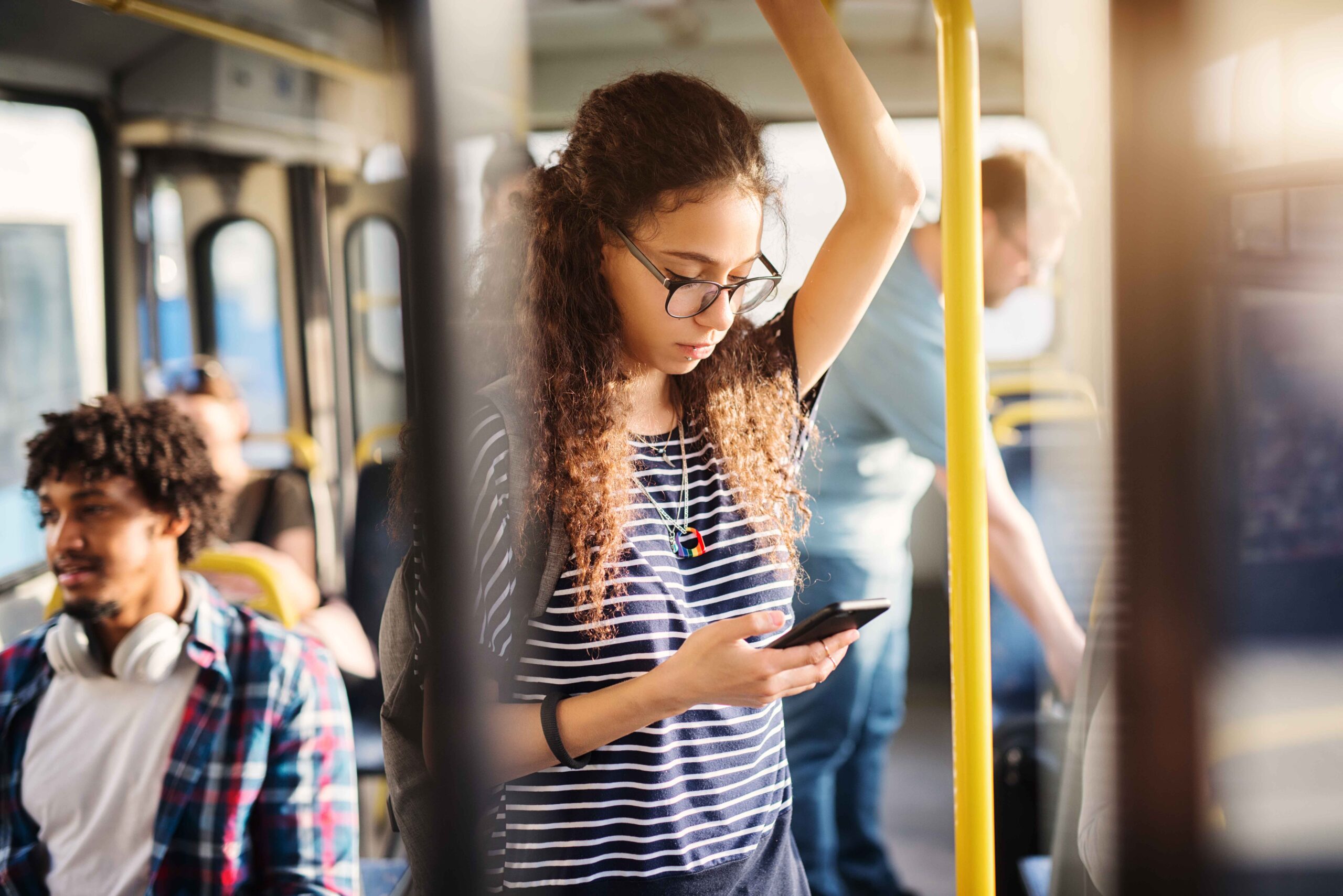 Menina negra segurando na barra do ônibus com o celular na mão